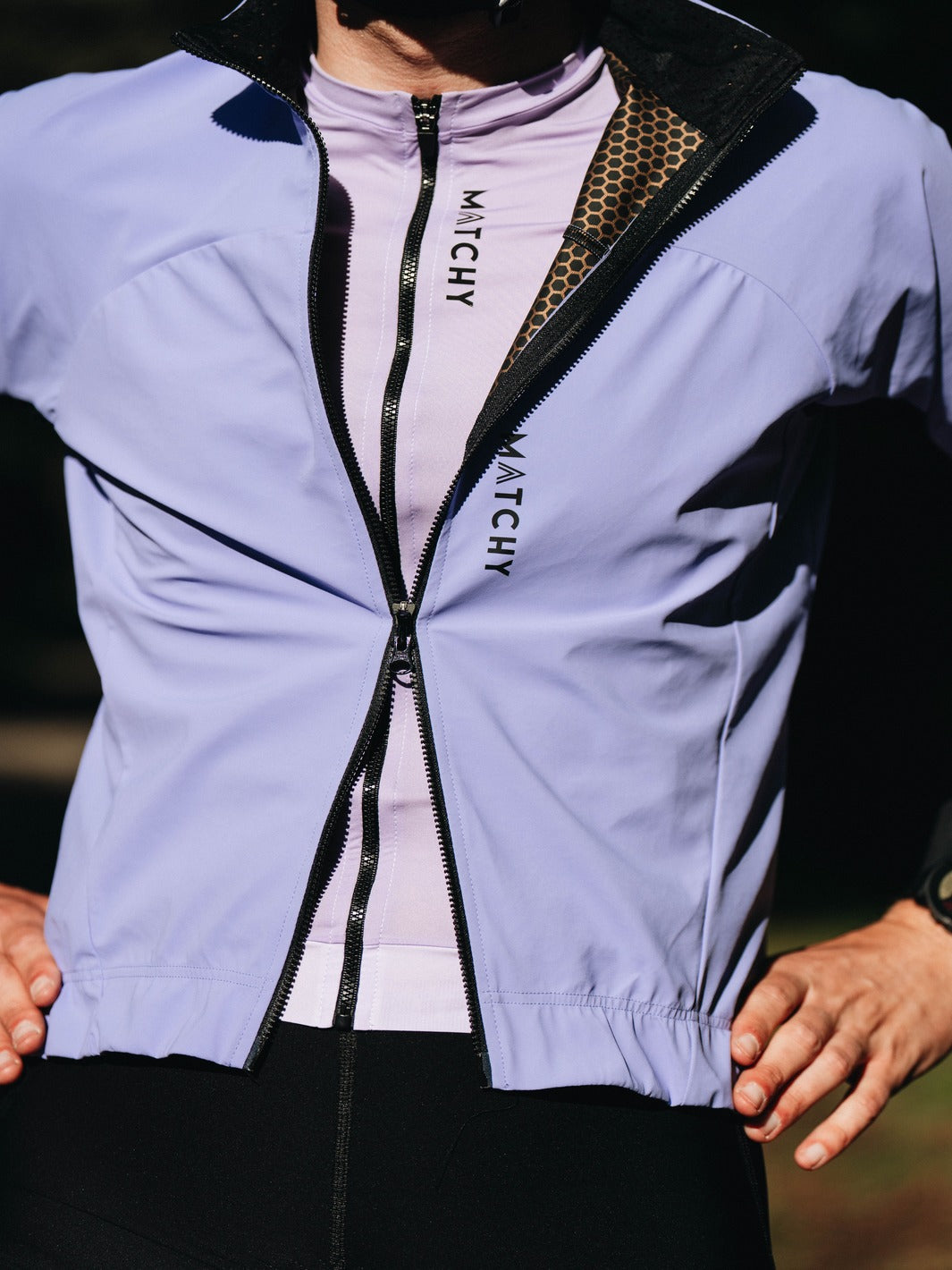 Coupe-vent vélo MATCHY coloris lavande porté par un cycliste équipé d'un casque blanc et lunettes de soleil, zip central et poignets ajustés.