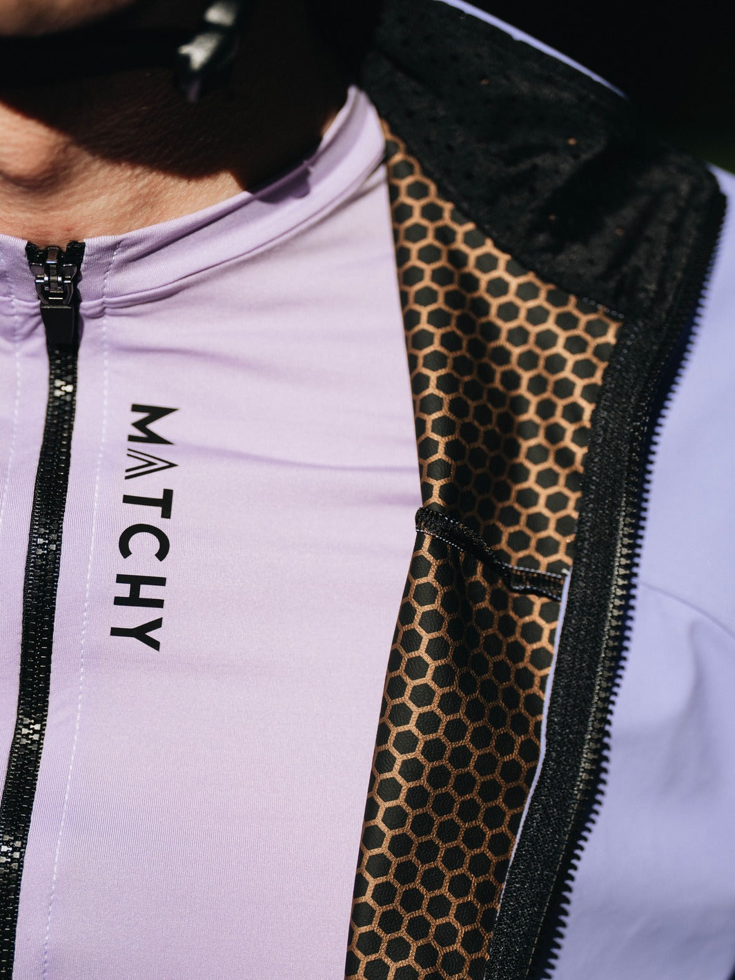 Coupe-vent vélo MATCHY coloris lavande porté par un cycliste équipé d'un casque blanc et lunettes de soleil, zip central et poignets ajustés.