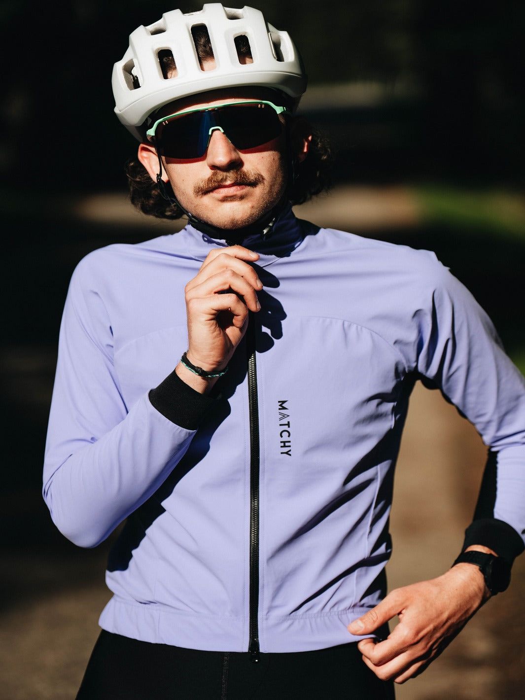 Coupe-vent vélo MATCHY coloris lavande porté par un cycliste équipé d'un casque blanc et lunettes de soleil, zip central et poignets ajustés