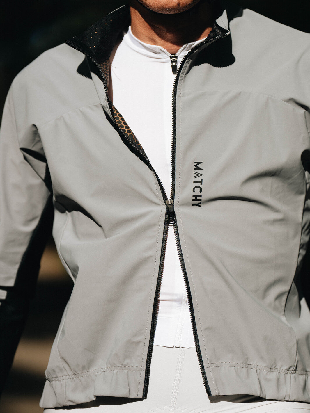 Coupe-vent vélo MATCHY coloris gris porté par un cycliste équipé d'un casque blanc et lunettes de soleil, zip central et poignets ajustés.